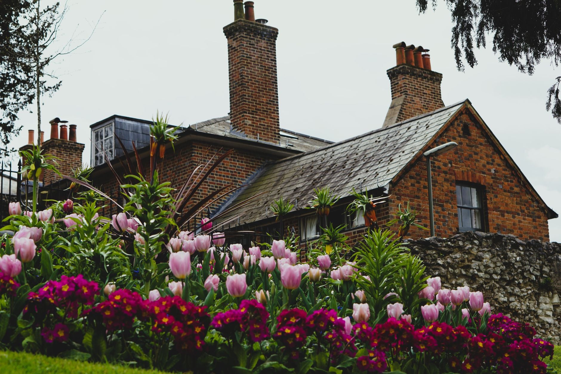 Charming brick cottage surrounded by colorful spring flowers in a lush garden.
