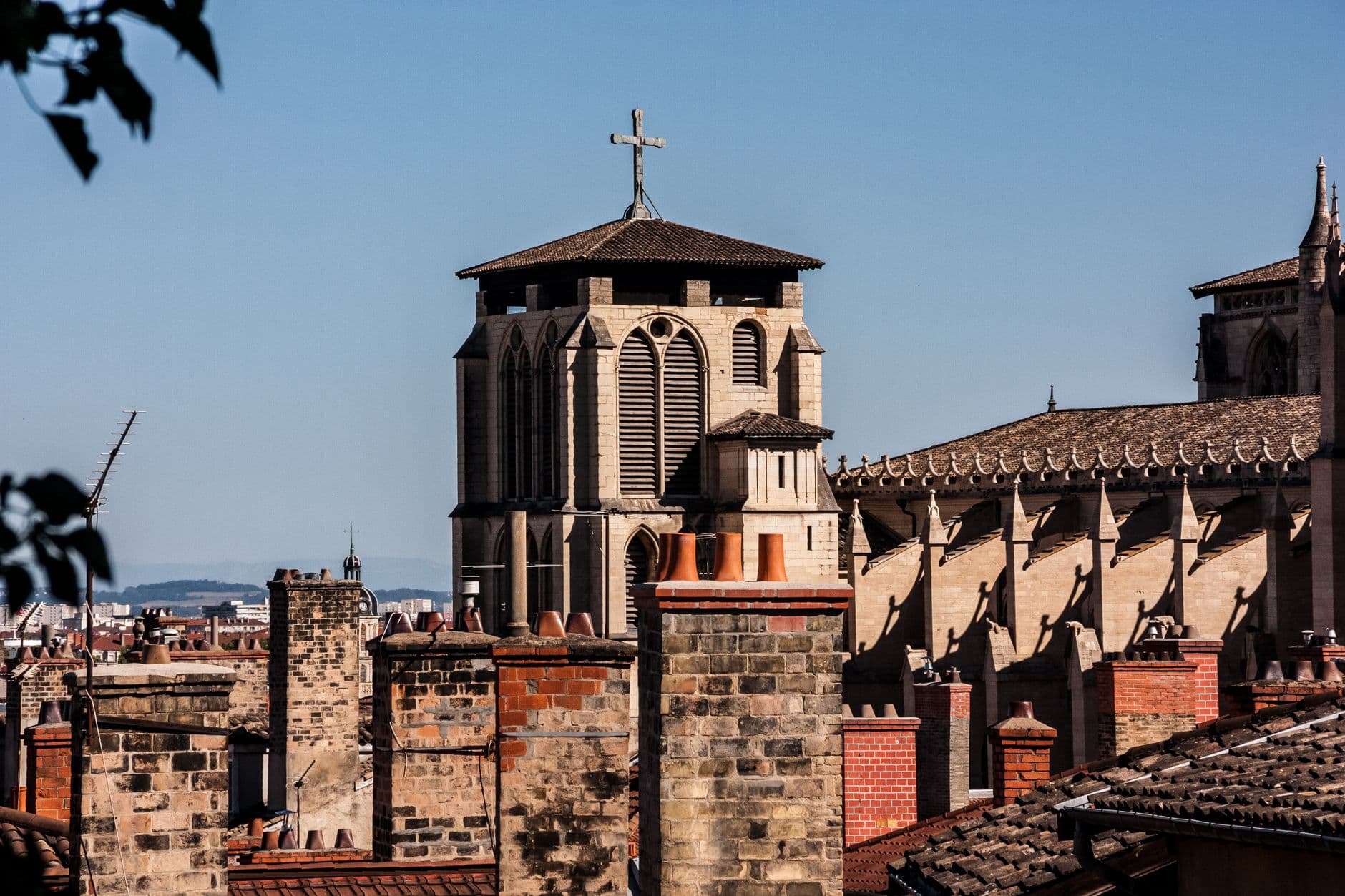 View of a historic church facade in Lyon, featuring a cross and traditional rooftops against a blue sky.